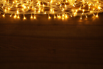 Beautiful glowing Christmas lights on wooden table, top view. Space for text