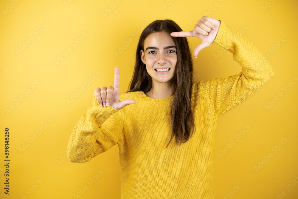 Pretty girl wearing a yellow sweater standing over isolated yellow background smiling making frame with hands and fingers with happy face Pretty girl wearing a yellow sweater standing over isolated yellow background smiling making frame with hands and fingers with happy face