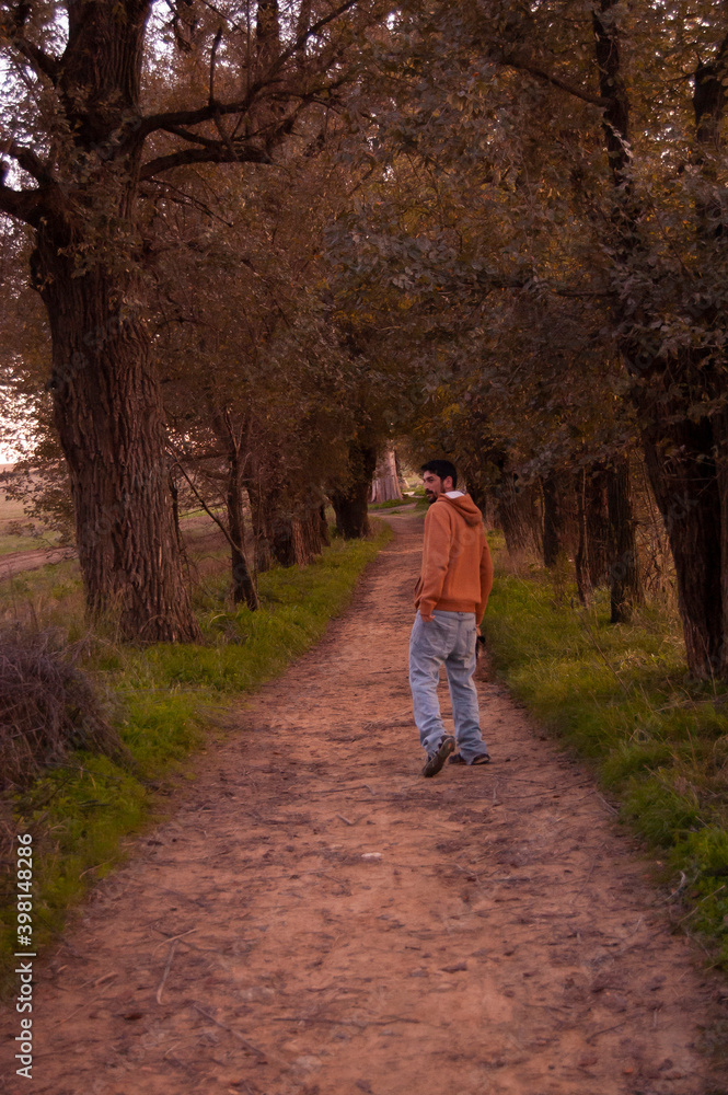 young man in the forest at autumn with a yellow hoodie and blue jeans