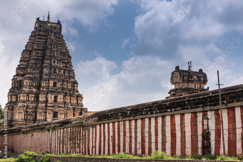 Hampi, Karnataka, India - November 4, 2013: Virupaksha Temple complex. Red and white wall around said complex under blue cloudscape. East and central gate Gopurams visible over it. photo