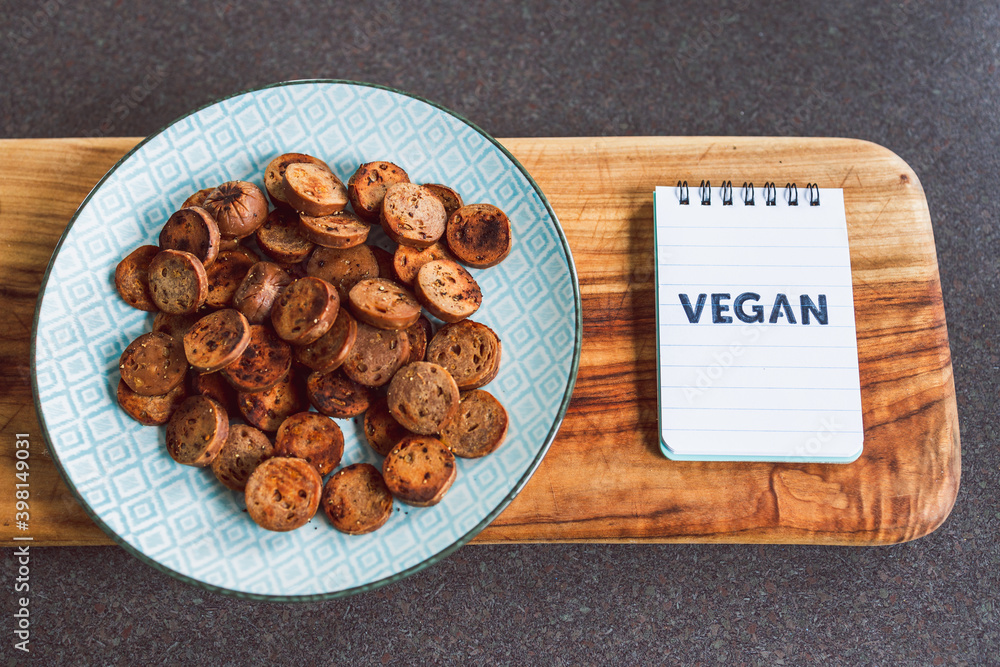 plant-based food, vegan sausage cut into salami slices and pan fried with cracked pepper on top next to memo with Vegan written on it plant-based food, vegan sausage cut into salami slices and pan fried with cracked pepper on top next to memo with Vegan written on it