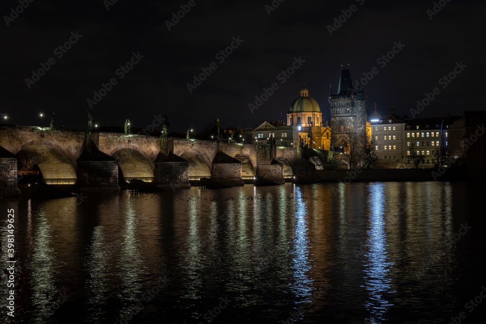 .Charles Bridge and lights from street lights are reflected on the surface of the Vltava River in the center of Prague at night in the Czech Republic