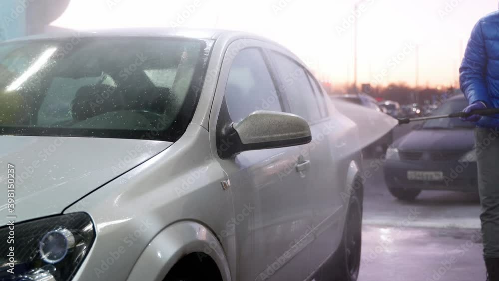 Young man in blue jacket wash grey car in self service automobile cleaning station with high pressure water and detergent soap Young man in blue jacket wash grey car in self service automobile cleaning station with high pressure water and detergent soap