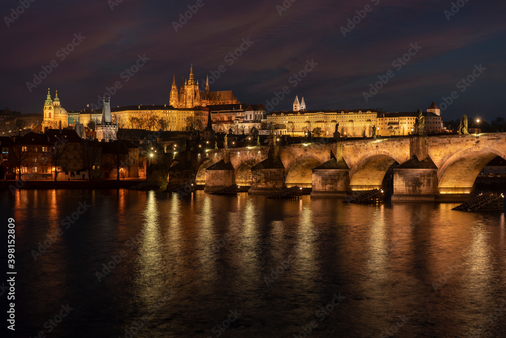 . prague castle and charles bridge and st. vita church lights from street lights are reflected on the surface of the vltava river in the center of prague at night in the czech republic