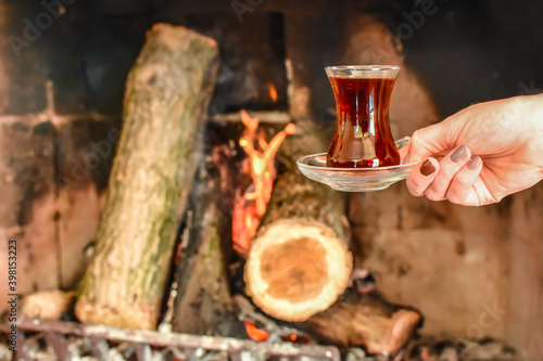 Closeup of cup with famous traditional Turkish tea in front cozy and worm fireplace, in country house. Winter or autumn (fall) vacation in Turkey. 
