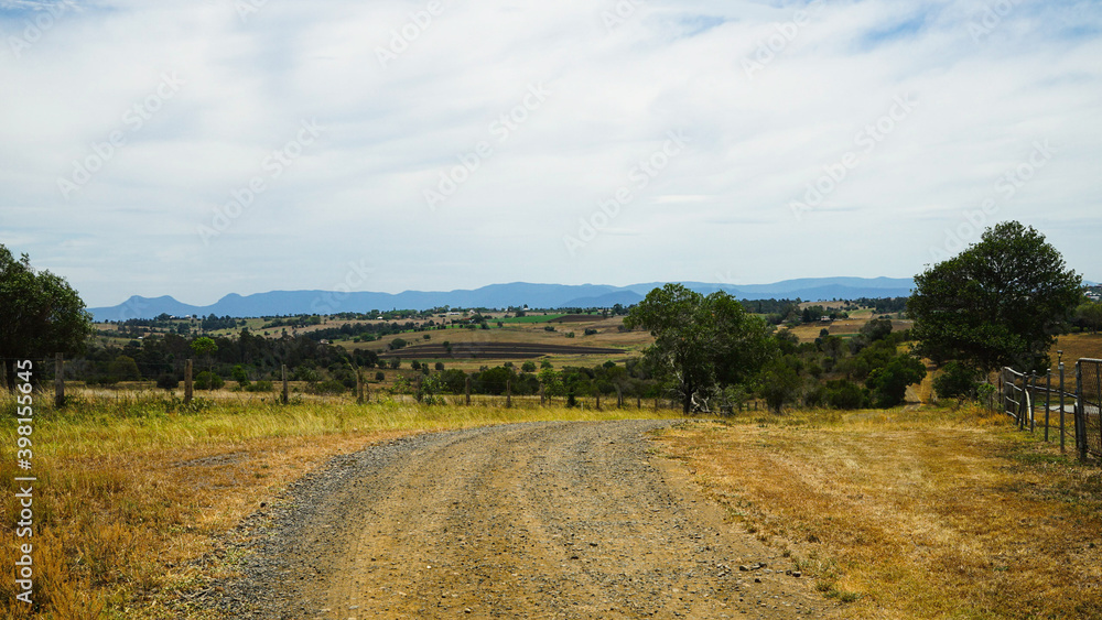 Fototapeta premium Panoramic rural landscape with gravel road in the foreground and mountains in the distance. Scenic Rim, Queensland, Australia.