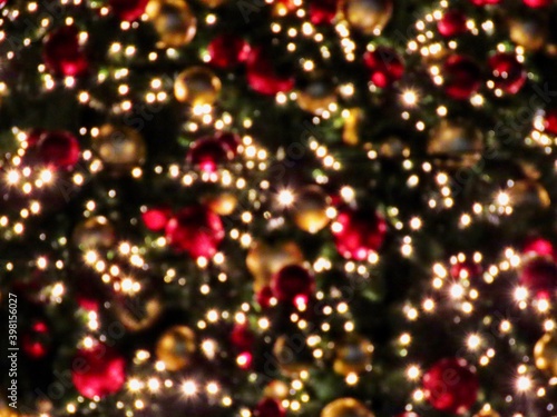 Defocused bokeh Christmas tree themed background with red and gold baubles, tree branches, small LED lights at night