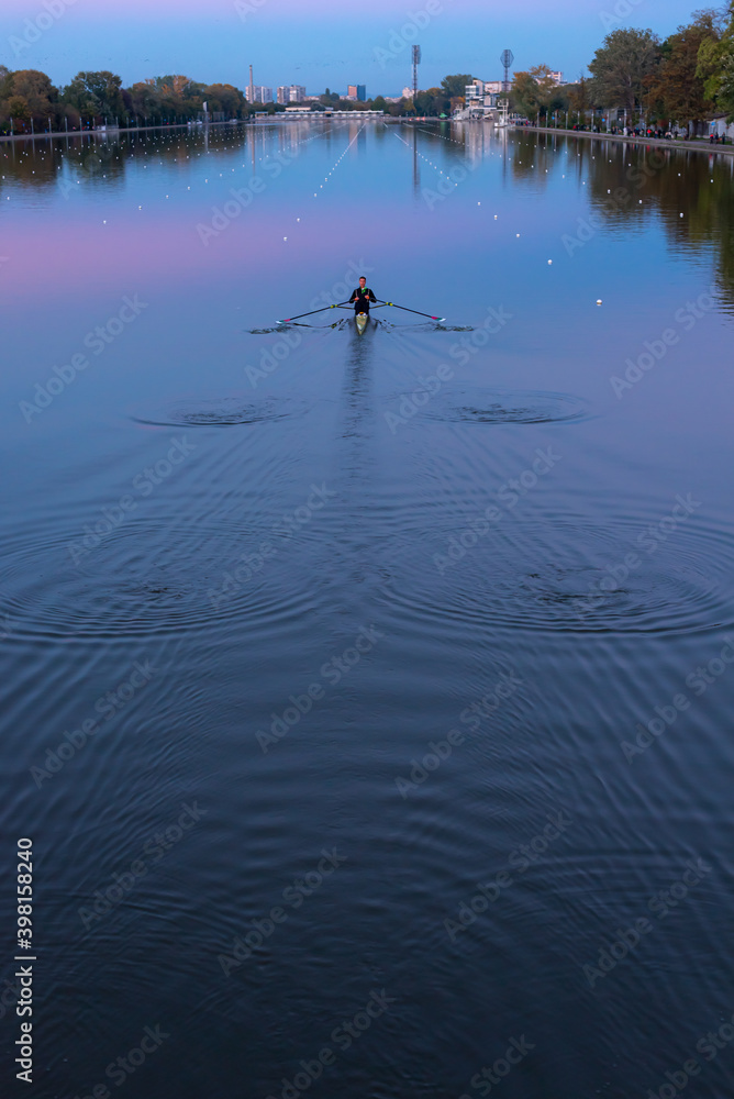 Lonely rowing boat sports in long canal training in calm sunset water with reflections and vibrant colors in Plovdiv, Bulgaria Lonely rowing boat sports in long canal training in calm sunset water with reflections and vibrant colors in Plovdiv, Bulgaria