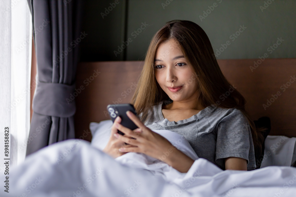 Beautiful long hair women play smartphone on the bed after wake up in the morning.