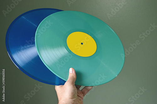 Someone honding some cool blue and turquoise vinyl records in a dark green background.