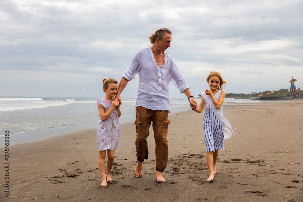 Father with daughters walking barefoot along the beach holding hands. Family relation. Vacation in Asia. Summer holidays. Happy family spending time together. Copy space. Bali island.