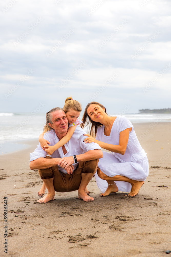 Daughter hugging father. Husband and wife hunkering down on the sand. Relation between parents and daughter. Family concept. Spend time together on the beach. Copy space. Bali, Indonesia Daughter hugging father. Husband and wife hunkering down on the sand. Relation between parents and daughter. Family concept. Spend time together on the beach. Copy space. Bali, Indonesia