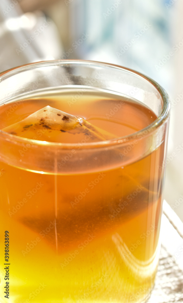 A beautiful glass filled with golden tea in the afternoon sunlight.