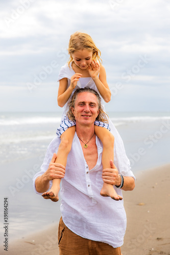 Daughter sitting on father's shoulders. Father and daughter playing together at the beach. Happy family. Having fun together. Quality time. Summer holiday. Family relation. Bali © Olga