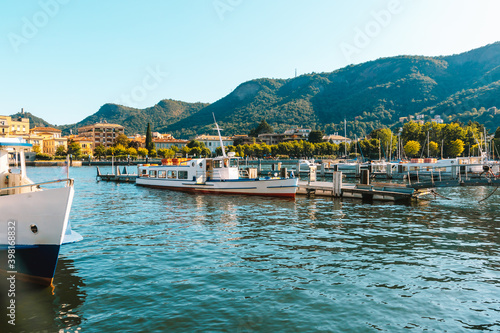 Como lake in city Como picturesque scenic view to blue water with white yachts and boats, mountains and city shore