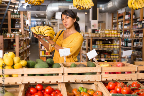 Woman shopper chooses ripe banana at grocery supermarket