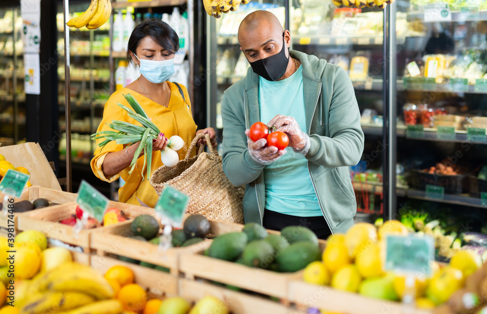 Married couple in protective mask choosing ripe tomatoes at grocery store