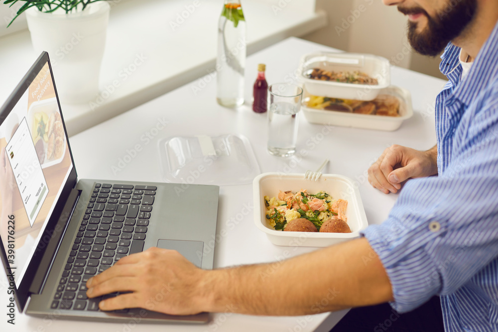 Man signing up for food delivery website using laptop while having lunch break in the office Man signing up for food delivery website using laptop while having lunch break in the office
