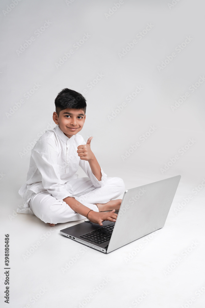 Cute indian boy using laptop and showing thumps up over white background Cute indian boy using laptop and showing thumps up over white background