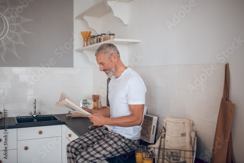 Grey-haired tall man reading a newspapaer and looking interested photo