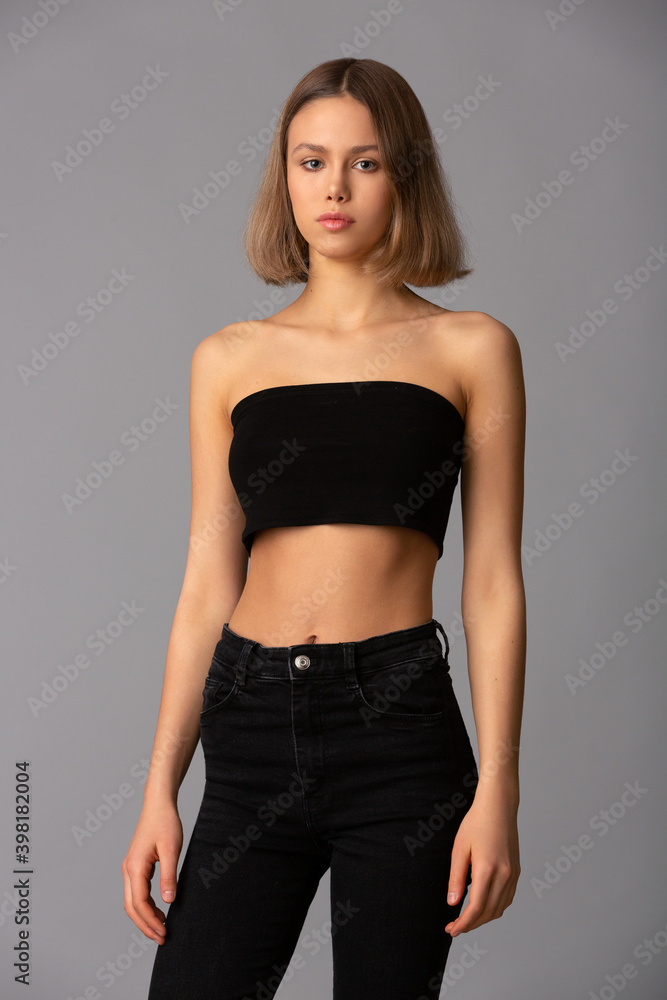 young girl with skillful makeup in a black short top and black leggings posing standing on a gray background young girl with skillful makeup in a black short top and black leggings posing standing on a gray background