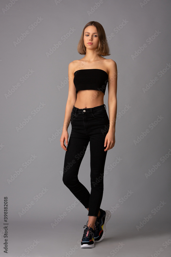 young girl with skillful makeup in a black short top and black leggings posing standing on a gray background young girl with skillful makeup in a black short top and black leggings posing standing on a gray background