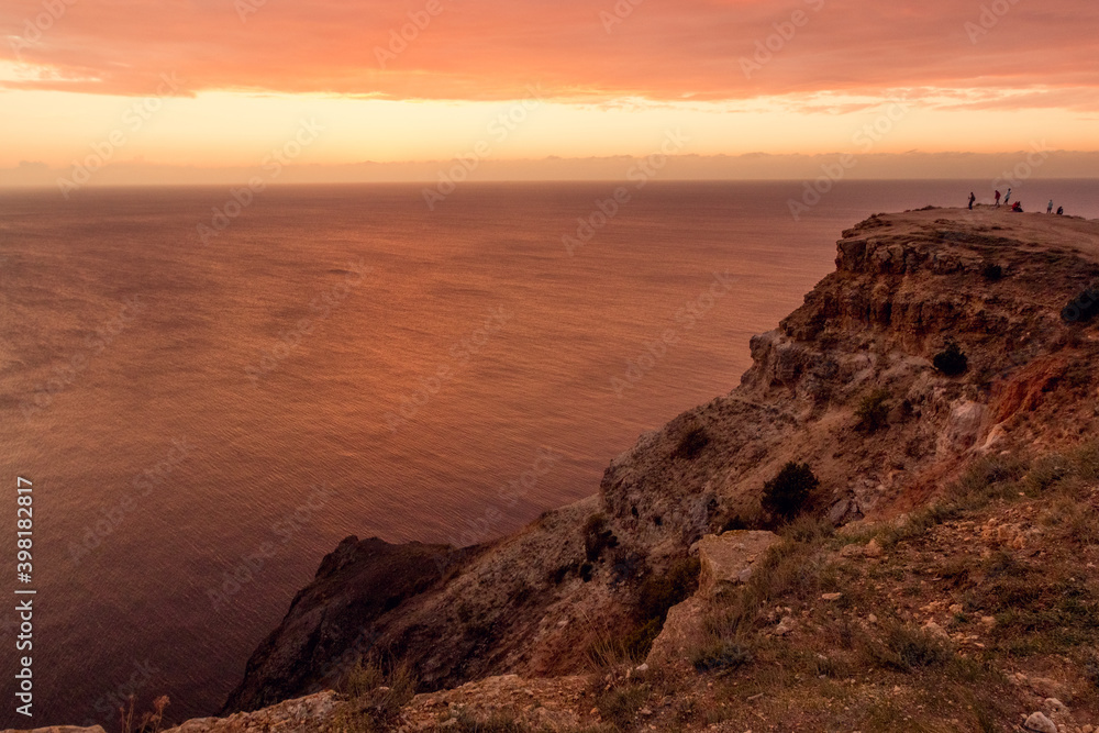 Seascape at red sunset. On the edge of a cliff. Summer-autumn. Horizontal photo. A soft picture. The view from the top