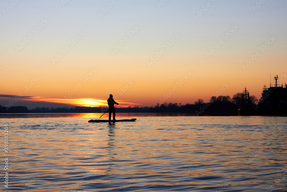 Silhouette of a man paddle boarding at winter river at sunset. Concept lifestyle sport