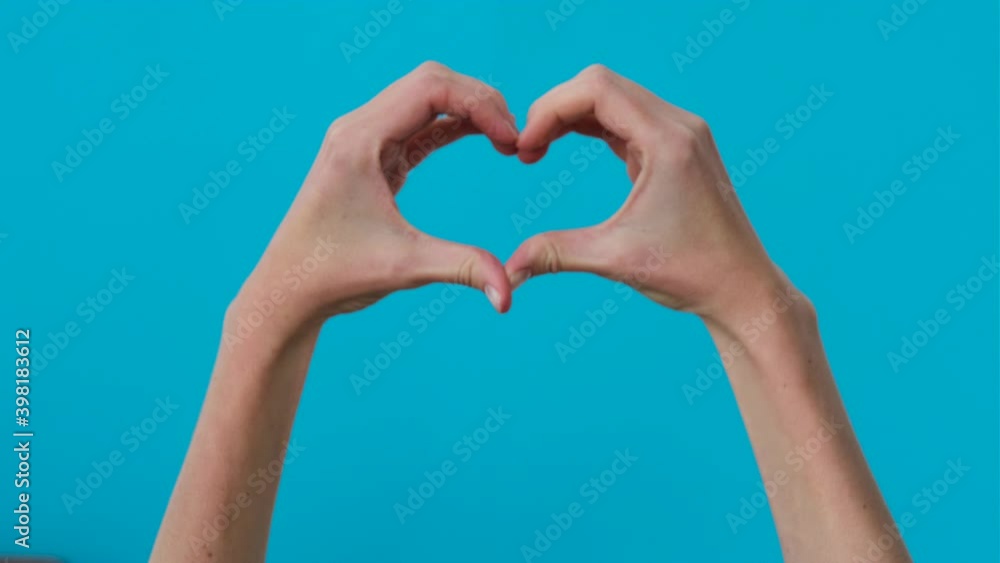 Hands of girl with folded fingers in shape of heart over blue background Hands of girl with folded fingers in shape of heart over blue background
