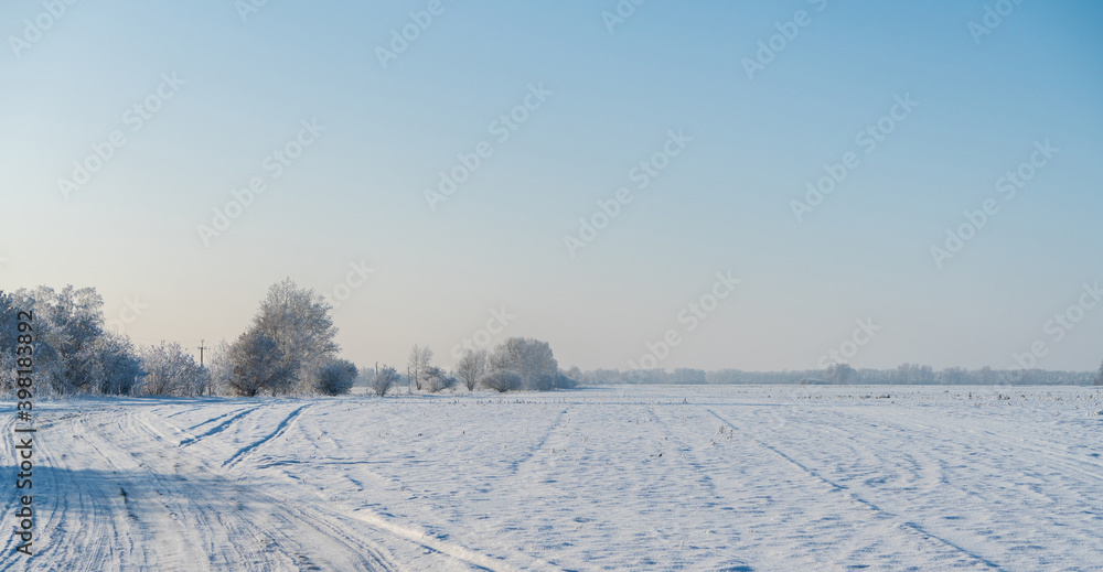 Snow covered winter field with trees and road going through to the horizon. Winter landscape. Beautiful winter nature. Snow covered winter field with trees and road going through to the horizon. Winter landscape. Beautiful winter nature.