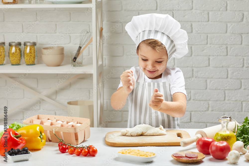 little child boy in chef hat and an apron cooking pizza in the kitchen little child boy in chef hat and an apron cooking pizza in the kitchen
