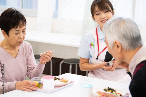 食事中の高齢の入居者たちと楽しく会話している介護施設の女性職員