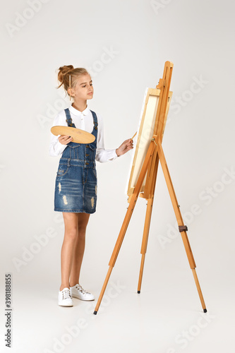 beautiful little girl holding a wooden art palette and brush on studio background. child painting. Full length