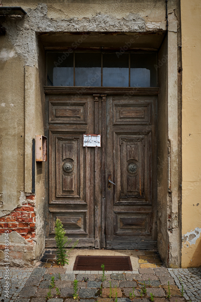 Fototapeta premium Verfallener Hauseingang mit Kassettentür in der Altstadt von Neuruppin. Schild mit verwitterter Inschrift: