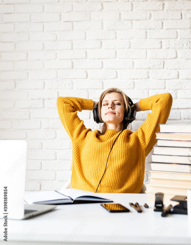 Young woman in black headphones sitting at the desk relaxing with her eyes closed after long study