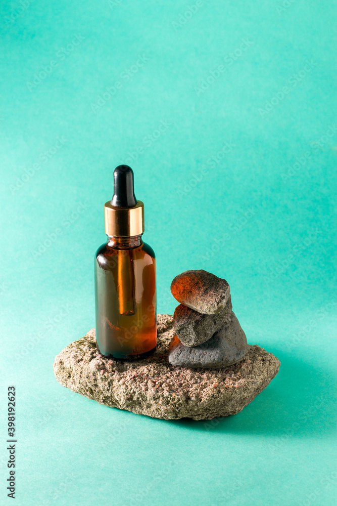 Amber beauty facial oil bottle next to the stones on the turquoise background close up isolated. Beauty concept. Connection with a nature concept. Natural beauty products concept. Skincare