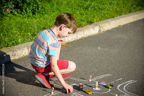 Funny kid boy having fun with picture drawing traffic car with chalks. Creative leisure for children outdoors in summer. Difficult traffic rules concept