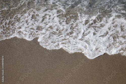 Surf on a sandy beach for background, aerial view. Empty sea coast with grey sand and clear water