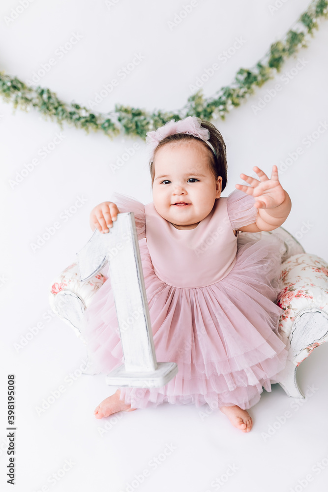 a little cute girl in a beautiful dress is sitting in a chair, holding the number 1 in her hand a little cute girl in a beautiful dress is sitting in a chair, holding the number 1 in her hand