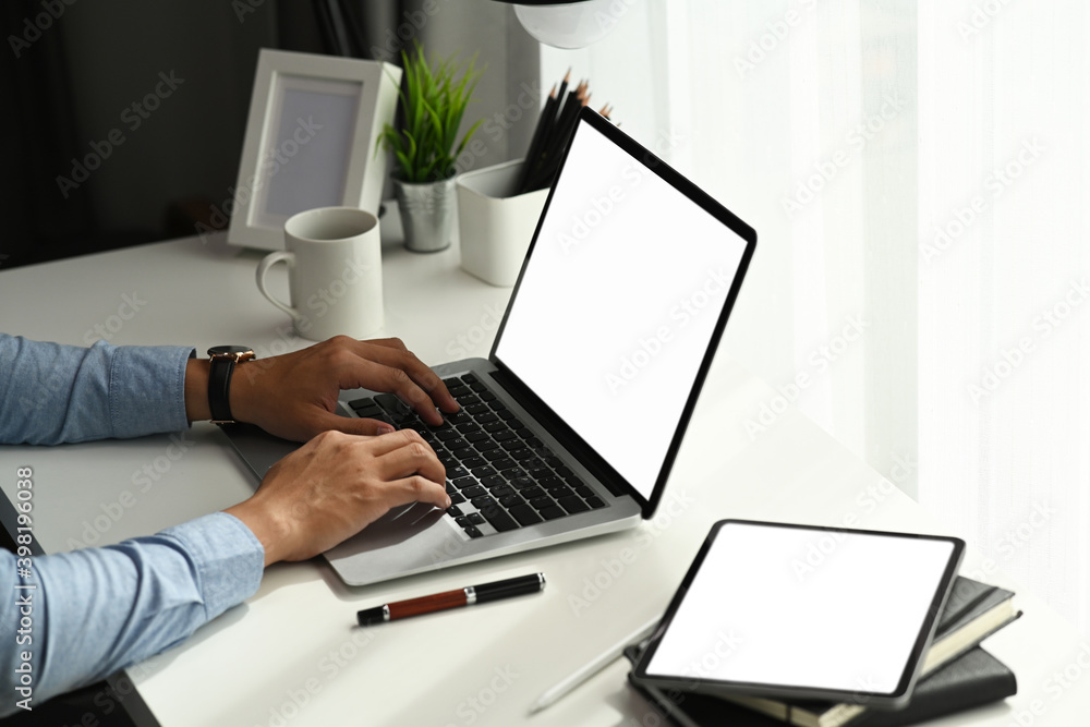 Young man hands working on laptop at comfortable workspace with blank screen tablet on desk. Young man hands working on laptop at comfortable workspace with blank screen tablet on desk.