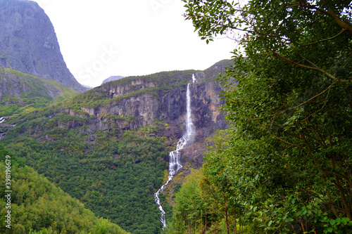 Norwegian mountain landscape with waterfall. Pathway to Briksdal or Briksdalsbreen glacier in Olden. Tree crown in the foreground.