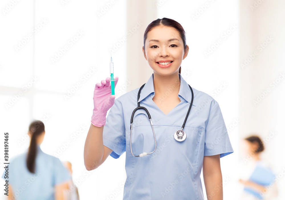 medicine, vaccination and healthcare concept - happy smiling asian female doctor or nurse in blue uniform with stethoscope and syringe over hospital background