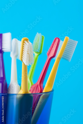 A group of colorful toothbrushes in a blue glass. Studio photo isolated on blue background. Selective focus on object. 