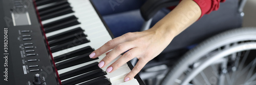 Woman in wheelchair is pressing piano keys close-up. Hobbies of people with disabilities concept.