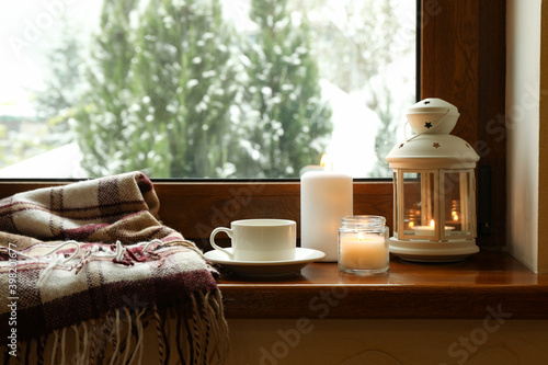 Fototapeta Plaid, cup, candles and lantern on wooden windowsill