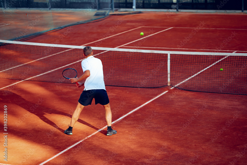 Back view of a man playing tennis on tennis court