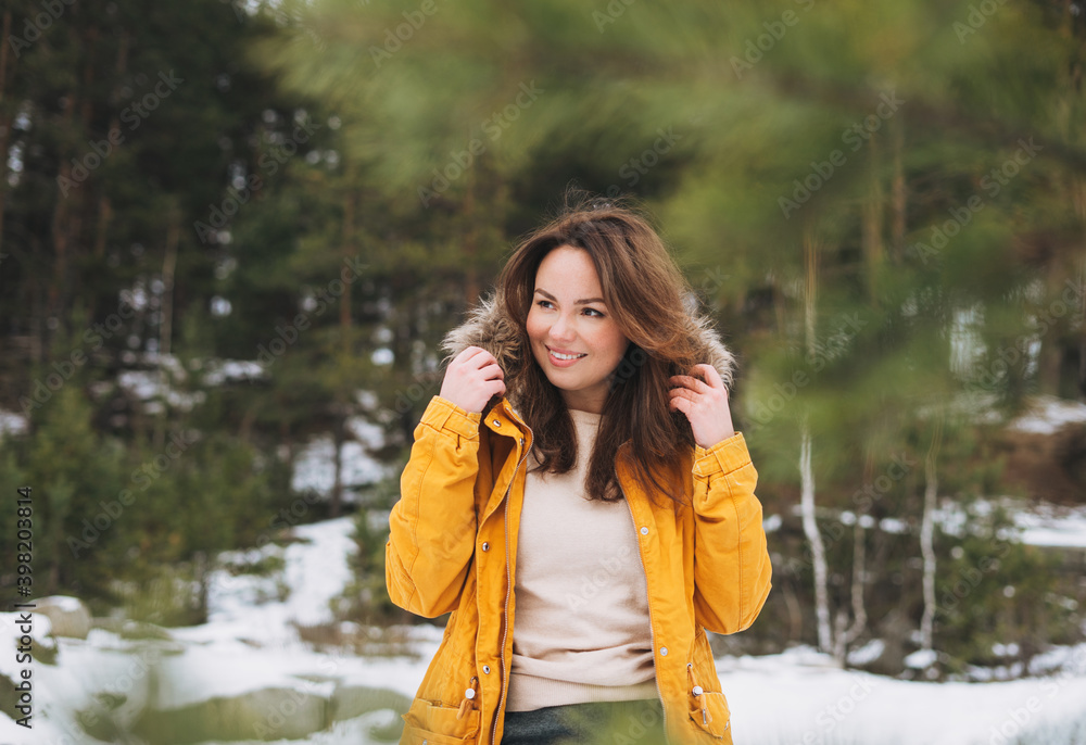 Portrait of young smiling beautiful woman in yellow jacket walking in the winter forest Portrait of young smiling beautiful woman in yellow jacket walking in the winter forest