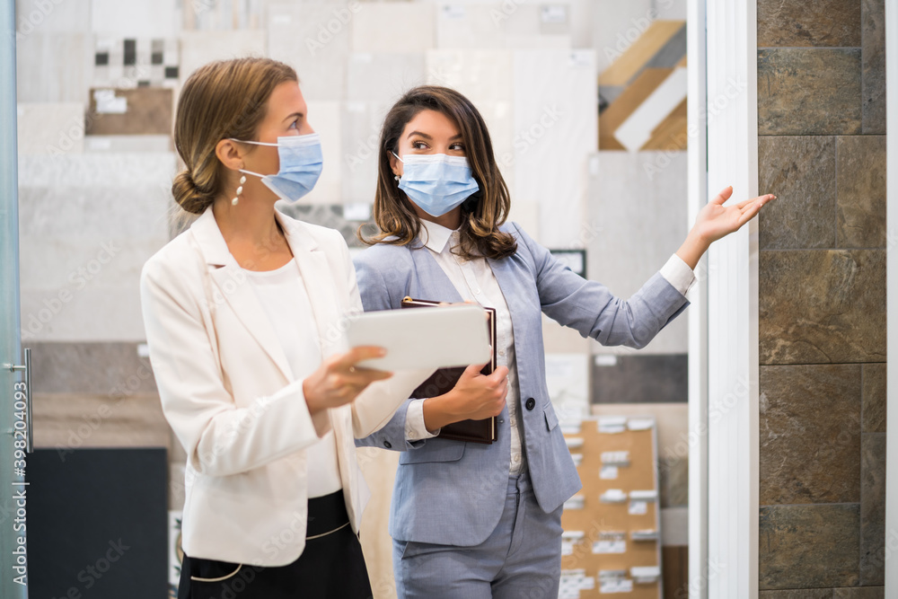 Businesswoman owning small business bath store. She is talking with a customer who is choosing the goods. They are wearing protective face mask. Businesswoman owning small business bath store. She is talking with a customer who is choosing the goods. They are wearing protective face mask.