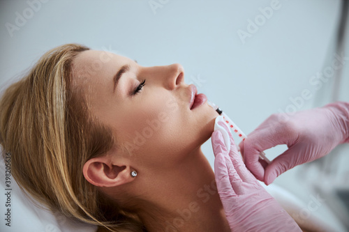 Professional cosmetologist injecting a dermal filler into the patient lips photo