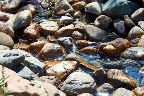 Springwater flow on the small pebbles on a sunny day with bright reflections. Nature backgrounds